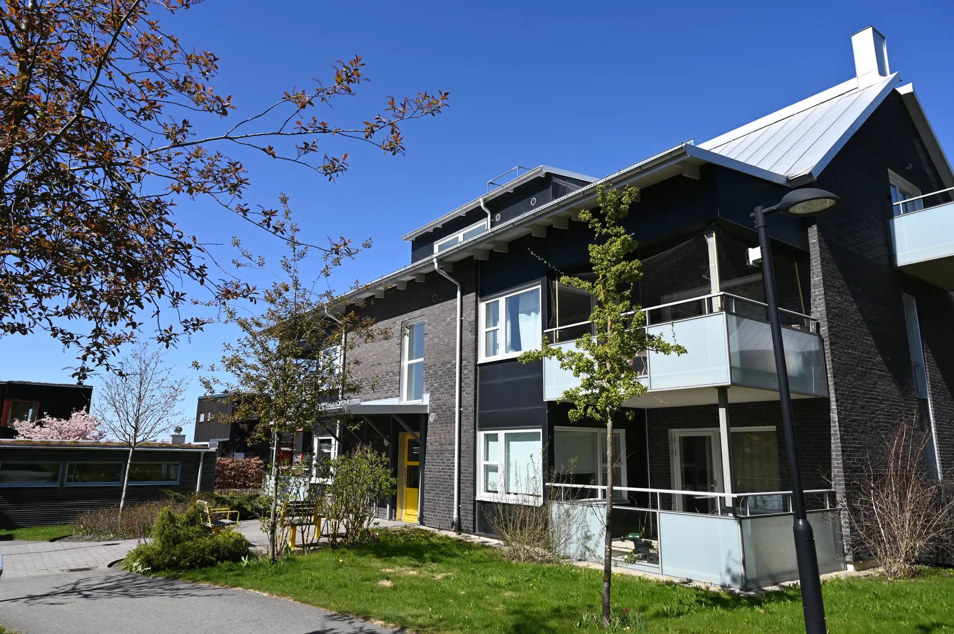 Modernt, svart flerbostadshus med balkonger, gräsmatta och träd längs gångväg